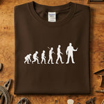 Evolution of Man mekaniker t-skjorte med evolusjonsdesign i hvitt på brun bakgrunn.