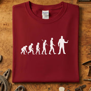 Evolution of Man mekaniker t-skjorte med stilisert design på burgunder bakgrunn.